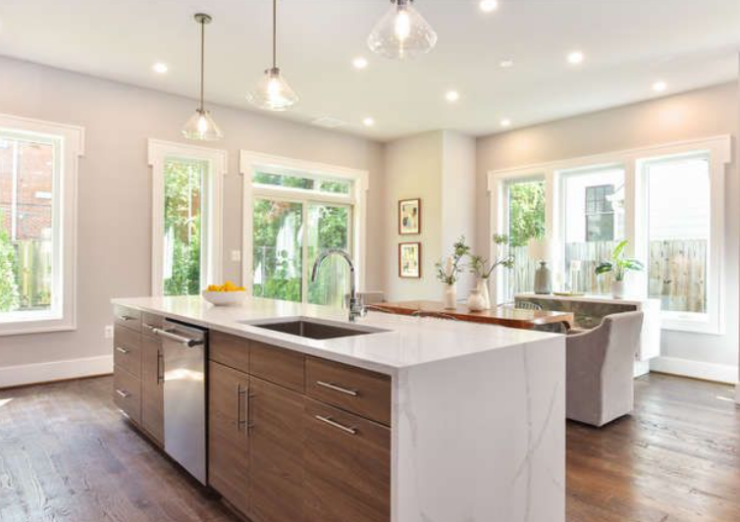 Modern kitchen with a large marble island, undermount sink, and built-in dishwasher; warm wood cabinets and wide windows flood the space with natural light.