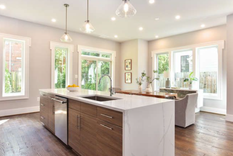 Modern kitchen with a large marble island, undermount sink, and built-in dishwasher; warm wood cabinets and wide windows flood the space with natural light.